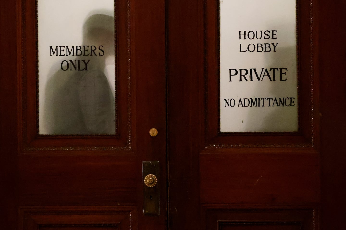 People are silhouetted behind closed doors inside a lawmakers-only hallway off the House chamber.